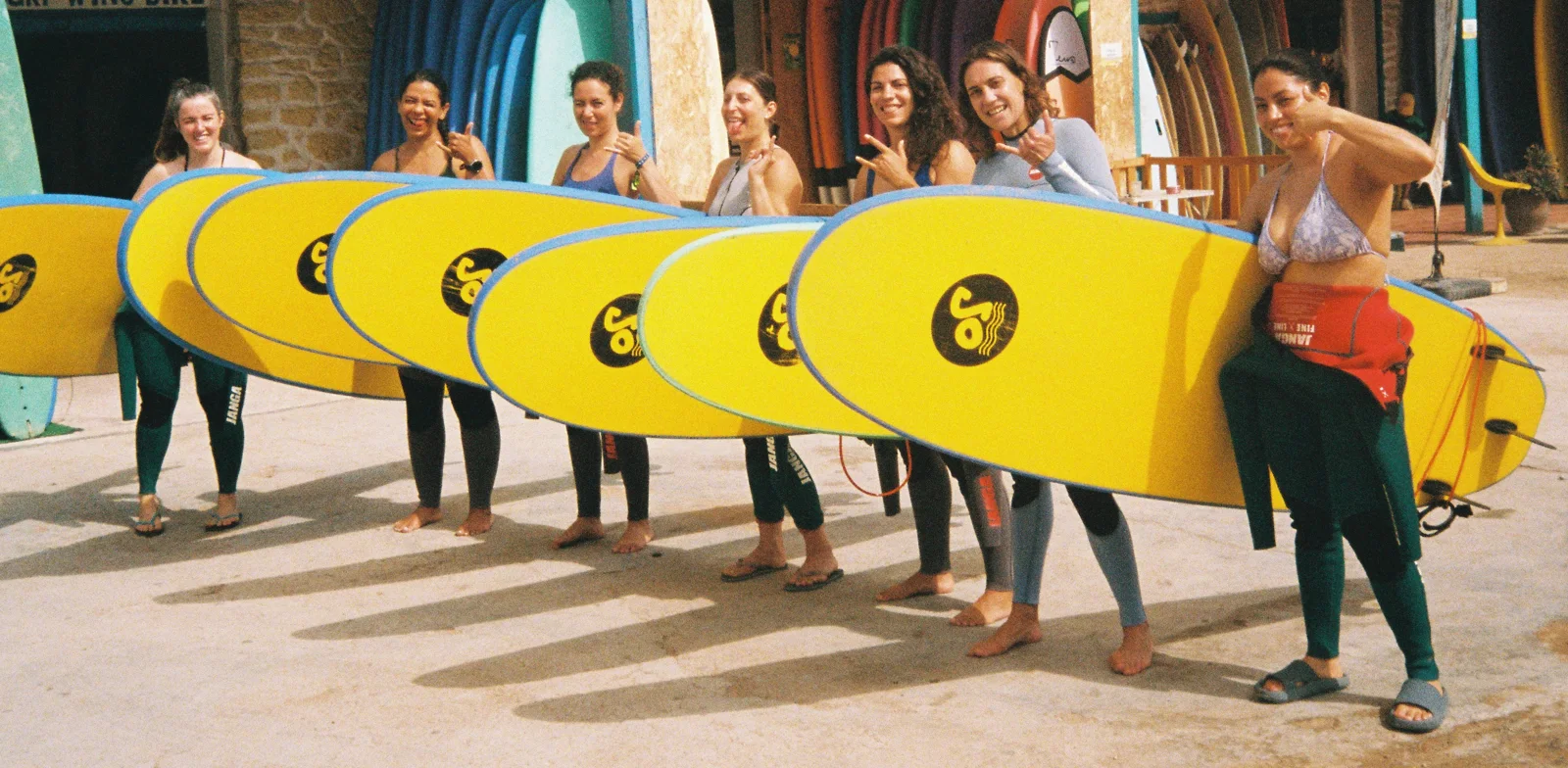 Group of smiling surfers holding yellow soft-top boards after a lesson