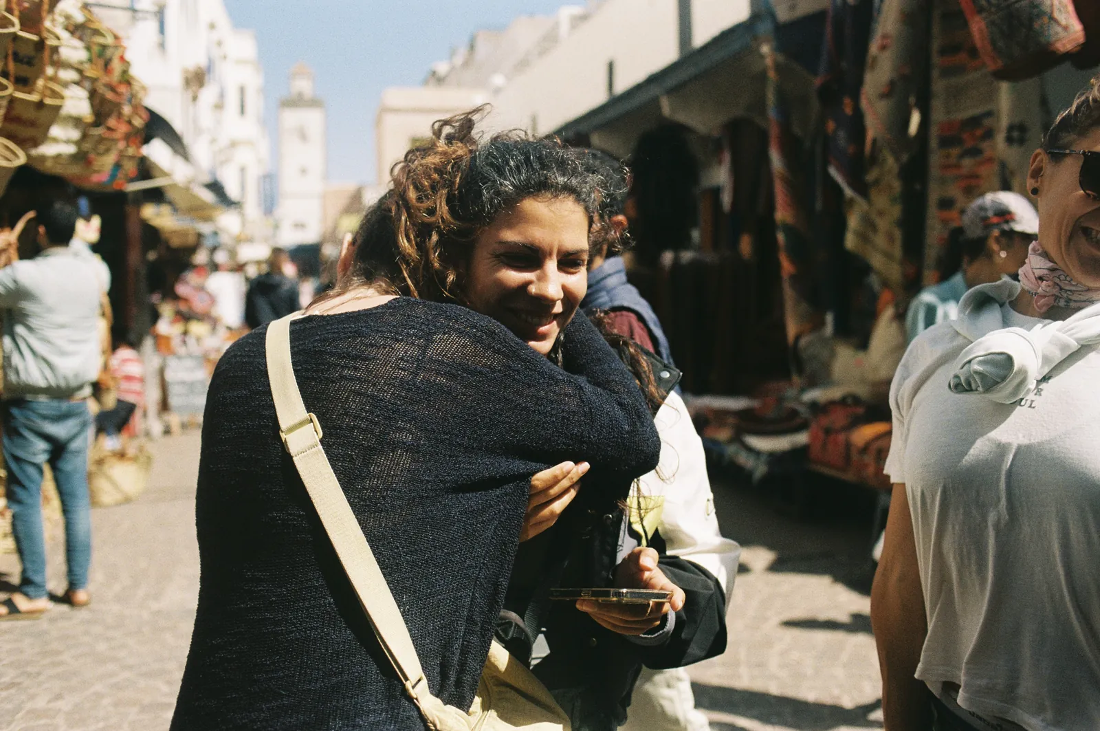 Two friends laughing in a busy medina street, a white clock tower behind