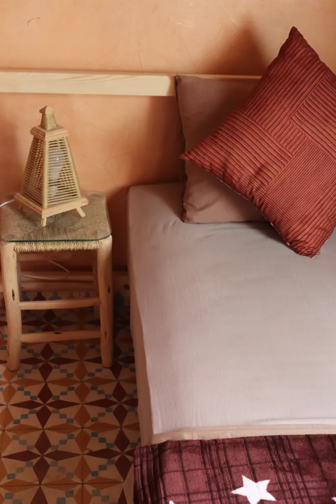 Single bed with a red cushion and a straw lamp