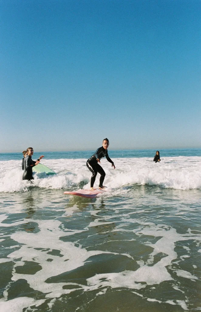 Smiling surfer riding the white water on a pink soft-top, friends cheering behind