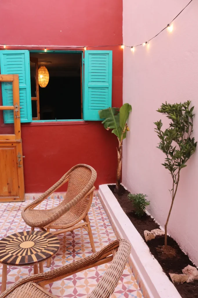 Riad courtyard in Tamraght with a red wall, turquoise shutters and wicker chairs