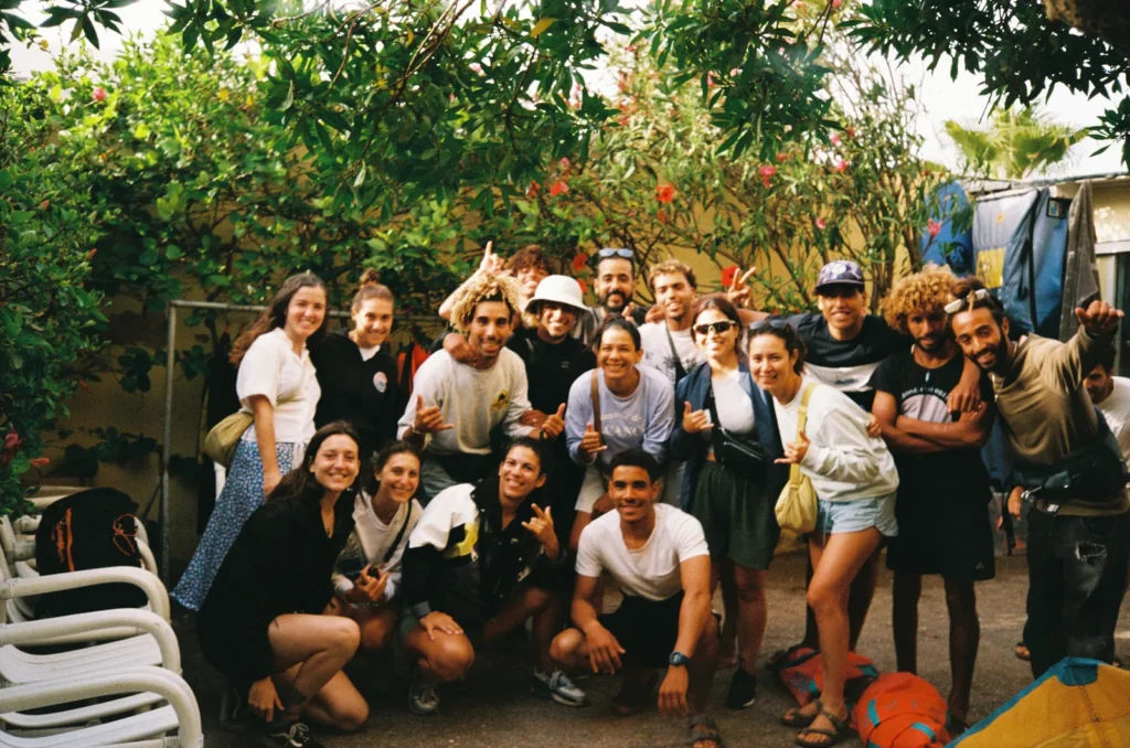 Big group of guests and surf instructors smiling and throwing shakas together in a leafy courtyard
