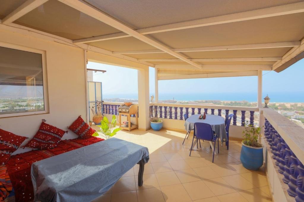 Le toit-terrasse du riad à Tamraght avec vue sur la mer, des coussins et un thé à la menthe prêts pour une pause au coucher du soleil